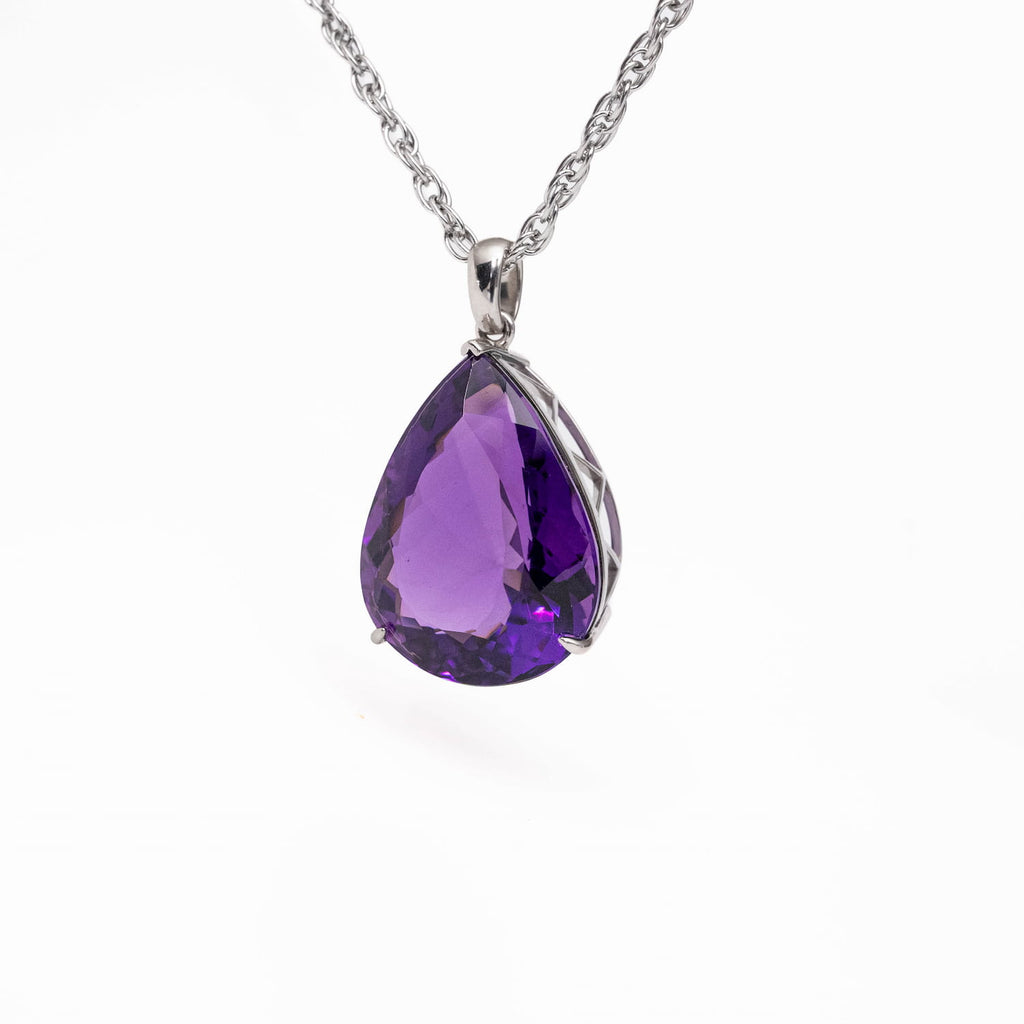 A teardrop-shaped purple amethyst gemstone pendant in a silver-toned metal setting on a silver chain, shown against a plain white background.