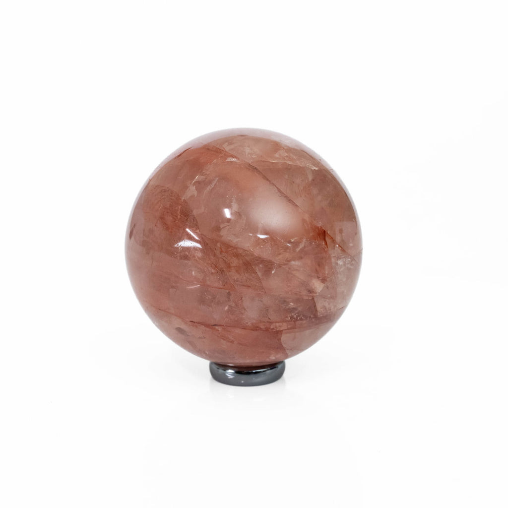 A polished reddish-brown quartz crystal sphere resting on a small black circular base, photographed against a seamless white background.