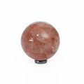 A polished reddish-brown quartz crystal sphere resting on a small black circular base, photographed against a seamless white background.
