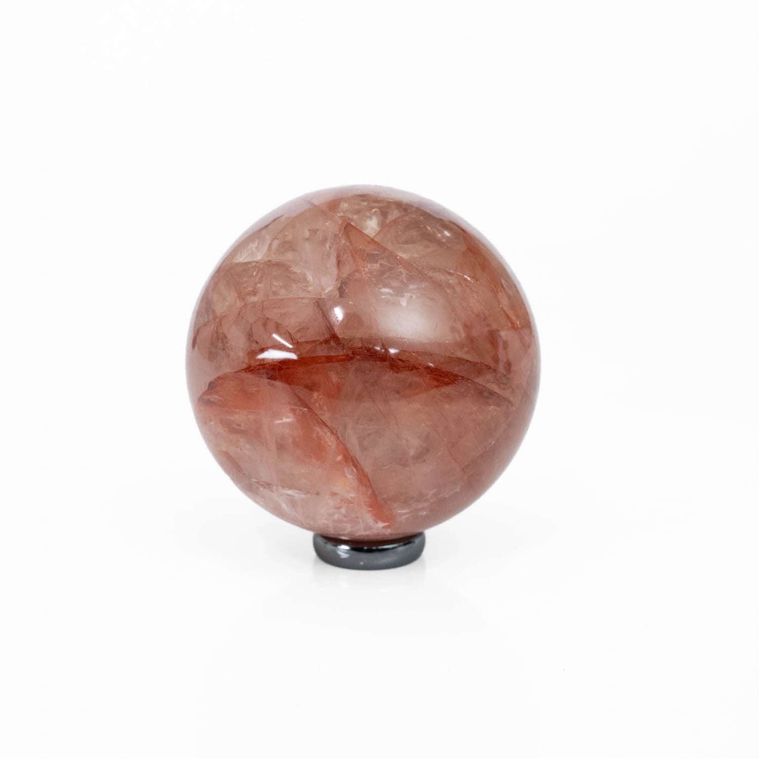 A polished reddish-brown quartz crystal sphere resting on a small black hematite base, photographed against a seamless white background.