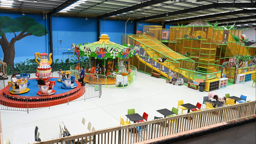 Indoor playground with spinning teacups ride and Madagascar carousel equipment and a dining area.